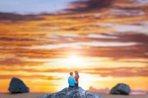 personnes miniatures, couple assis sur une plage de la mer avec fond de coucher de soleil photo