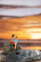 personnes miniatures, couple assis sur une plage de la mer avec fond de coucher de soleil photo