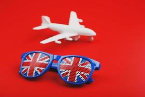 avion blanc et lunettes de soleil avec le drapeau du royaume-uni sur fond rouge. Voyager en Angleterre. photo