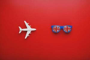 avion blanc et lunettes de soleil avec le drapeau du royaume-uni sur fond rouge. Voyager en Angleterre. photo