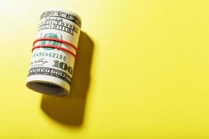 un rouleau de billets américains de cent dollars est attaché avec une bande élastique rouge sur fond jaune. photo