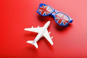 un avion de passagers blanc vole dans des lunettes de soleil avec le drapeau du royaume-uni, sur fond rouge. photo