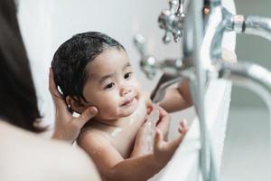 asiatique mignon enfant fille enfant en bas âge ayant un bain se laver les cheveux nettoyer la baignoire de bain avec sa mère. l'amour et les soins de la mère heureuse petite fille innocente s'amusent à jouer avec de l'eau en profitant. notion de bébé. photo