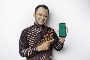 portrait d'un homme asiatique souriant portant une chemise batik et montrant un écran vert sur son téléphone, isolé sur fond blanc photo