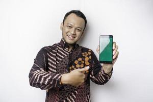 portrait d'un homme asiatique souriant portant une chemise batik et montrant un écran vert sur son téléphone, isolé sur fond blanc photo