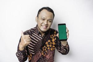 portrait d'un homme asiatique souriant portant une chemise batik et montrant un écran vert sur son téléphone, isolé sur fond blanc photo