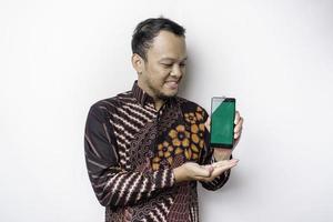portrait d'un homme asiatique souriant portant une chemise batik et montrant un écran vert sur son téléphone, isolé sur fond blanc photo