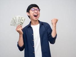 jeune homme asiatique tenant de l'argent montrer le poing en l'air heureux de gagner de l'argent photo