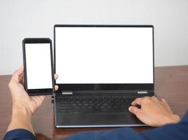 homme tenant un écran blanc vierge de téléphone portable avec une maquette d'écran blanc d'ordinateur portable sur la table photo