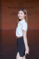 portrait d'un étudiant thaïlandais adulte en uniforme d'étudiant universitaire. belle fille asiatique debout confiant sur un fond de brique. photo