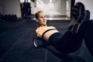 jeune sportive avec para-capacité faisant des exercices de relaxation avec un rouleau en mousse dans une salle de sport. photo