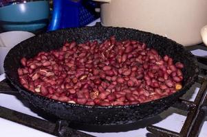 faire frire des cacahuètes, la main d'une femme remuant des cacahuètes dans une poêle à frire, gros plan. photo