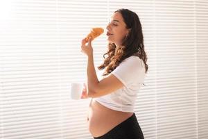 femme enceinte heureuse avec des petits pains croissants à la maison. concept de grossesse, de manger et de personnes photo