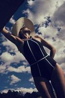 portrait d'une femme en maillot de bain, chapeau et lunettes de soleil en été sur la berge contre le ciel photo