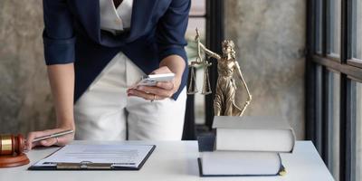 séduisante jeune avocate ou femme d'affaires parlant au téléphone et des avocats discutant des documents contractuels avec une échelle en laiton sur un bureau en bois au bureau. droit, services juridiques, conseil, justice et concept immobilier photo