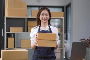 portrait d'une jeune femme asiatique travaillant une PME avec une boîte à la maison sur le lieu de travail. propriétaire de petite entreprise en démarrage, PME entrepreneur de petite entreprise ou entreprise indépendante en ligne et concept de livraison. photo
