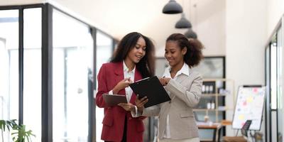 souriant diverses collègues femmes d'affaires travaillant ensemble sur un ordinateur portable, regardant l'écran, se tenant au bureau au bureau, les employés discutant de la stratégie du projet, partageant des idées photo