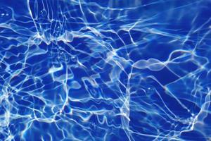 défocalisation floue transparente bleu clair texture de surface de l'eau calme avec des éclaboussures et des bulles. fond de nature abstraite à la mode. vagues d'eau au soleil avec caustiques. l'eau bleue qui brille photo