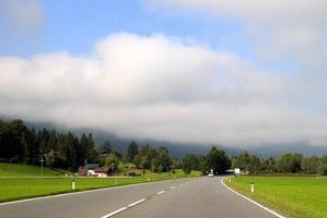 voyage à sankt-wolfgang, autriche. la route entre les vertes prairies avec les montagnes dans les nuages en arrière-plan par temps ensoleillé. photo