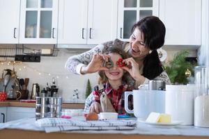 maman et fille dans la cuisine blanche préparent des biscuits pour noël et le nouvel an. journée familiale, préparation pour les vacances, apprendre à cuisiner de délicieuses pâtisseries, découper des formes dans la pâte avec des moules photo