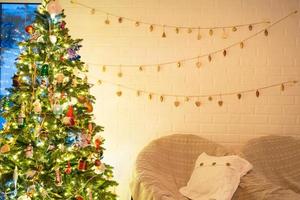 arbre de noël à l'intérieur blanc d'une maison aux murs de briques de style loft avec des guirlandes de jouets en verre sur une corde. décoration de guirlandes lumineuses de la salle du studio. maison confortable à noël et nouvel an photo