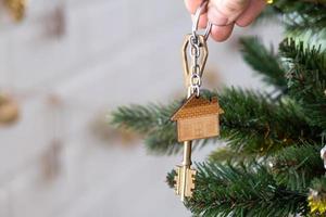 la clé de la maison avec un porte-clés est accrochée au sapin de noël. un cadeau pour le nouvel an, noël. construction, conception, projet, déménagement dans une nouvelle maison, hypothèque, location et achat immobilier. copie espace
