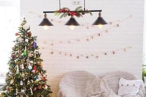 arbre de noël à l'intérieur blanc d'une maison aux murs de briques de style loft avec des guirlandes de jouets en verre sur une corde. décoration de guirlandes lumineuses de la salle du studio. maison confortable à noël et nouvel an photo