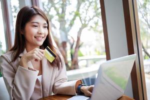 jolie femme d'affaires asiatique paiements achats en ligne par carte de crédit par ordinateur portable dans le café