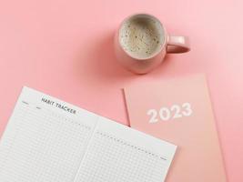 mise à plat du livre de suivi des habitudes sur un journal rose ou un planificateur 2023 et une tasse de café rose sur fond rose avec espace de copie. photo