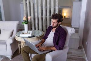 homme d'affaires sérieux au visage sérieux assis à la maison et utilisant un ordinateur portable pour son projet. indépendant travaillant à domicile concept homme d'affaires à la maison vérifiant les statistiques sur le téléphone portable et l'ordinateur portable photo