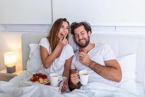 jeune couple marié amoureux prenant son petit déjeuner dans son lit. bonjour. petit déjeuner sain au lit. jeune beau couple d'amour prend son petit déjeuner au lit. photo