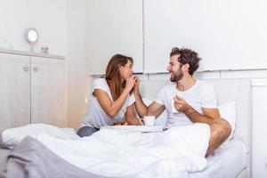 jeune bel homme nourrissant une jeune femme séduisante au lit le matin. petit déjeuner romantique pour deux. amour, soins, relations. couple prenant un petit déjeuner sain ensemble au lit à la maison photo