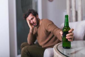 après le travail, un gars déprimé assis sur un canapé, buvant une bière froide. main tenant un verre, homme buvant seul à la maison. alcoolisme, dépendance à l'alcool et concept de personnes photo