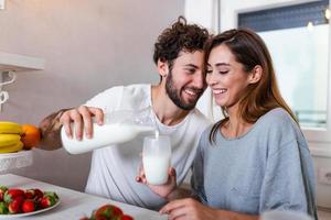 jeune couple souriant cuisinant des aliments dans la cuisine ensemble dans la cuisine, passant un bon moment ensemble. homme et femme riant et buvant du lait le matin avec petit déjeuner photo