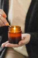 femme tenant à la main une bougie et une bougie allumée dans un petit bocal en verre ambré avec mèche en bois. concept zen et détente photo