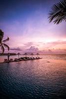 parasol et chaise autour de la piscine à débordement près de la plage de l'océan au lever ou au coucher du soleil. pour les voyages d'agrément et le concept de vacances, paysage de station balnéaire. vacances de détente tropicale, coucher de soleil photo