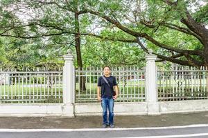 un t-shirt noir asiatique se tient devant une clôture vintage blanche à côté de la route dans l'après-midi. photo