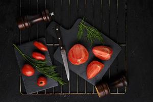ardoise de tomates tranchées, feuilles d'aneth, deux moulins à épices et couteau avec manche en bois sur le gril.