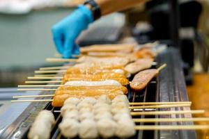 gros plan de boulettes de porc bâton de bois avec de petites saucisses grillées sur une cuisinière électrique à vendre sur le marché alimentaire. photo