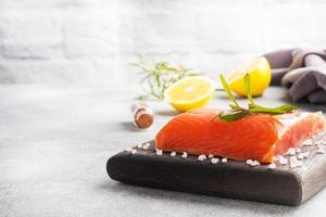 filet de saumon, poisson rouge salé sur une planche à découper en bois. citron, romarin épices. espace de copie. photo