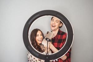 jeune couple de blogueurs de beauté, coiffeur, coiffeur et modèle avec coiffure shoot sur téléphone portable avec lampe annulaire sur le fond de mur gris photo