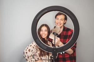 jeune couple de blogueurs de beauté, coiffeur, coiffeur et modèle avec coiffure shoot sur téléphone portable avec lampe annulaire sur le fond de mur gris photo