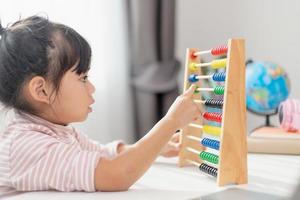 une jeune fille asiatique mignonne utilise le boulier avec des perles colorées pour apprendre à compter à la maison photo