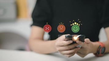 femme intelligente utilise un smartphone en choisissant l'icône de visage de sourire heureux vert. évaluation des commentaires et expérience positive des commentaires des clients, enquête de satisfaction. évaluation de la santé mentale. concept de la journée mondiale de la santé mentale photo