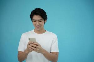 bel homme asiatique souriant heureux avec son téléphone sur fond bleu clair. photo