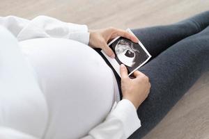une femme enceinte regarde une photo échographique du fœtus. la mère touche doucement le bébé sur le ventre. les femmes sont enceintes depuis 30 semaines. premier amour dans le ventre et dernière grossesse à terme