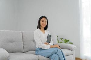 femme d'affaires asiatique souriante et tenant un livre au bureau. belle et belle femme asiatique est assise sur le canapé. portraits féminins. photo