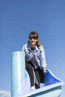 une femme infantile et heureuse assise sur un toboggan pour enfants sur une aire de jeux photo