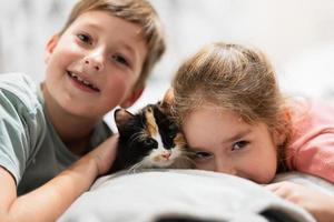 frère et soeur avec chat minou allongé sur le canapé. l'amour des enfants pour les animaux. photo