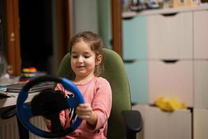 fille assise sur une chaise avec le volant d'un enfant dans ses mains dans la chambre des enfants. photo